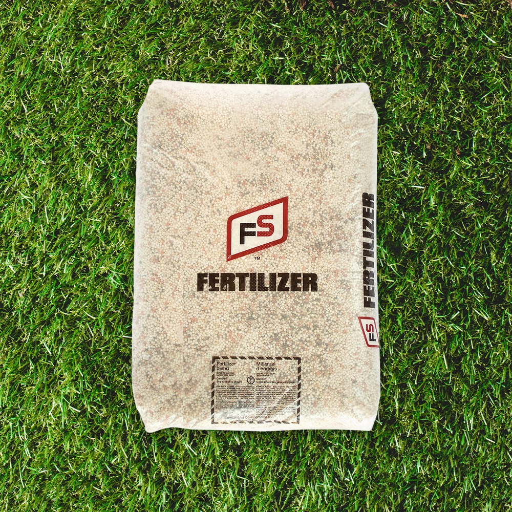 A bag of FS fertilizer lies on green grass, displaying logo and text, with small details visible on the packaging.